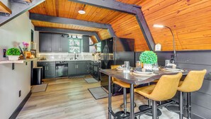 Eine moderne Küche mit dunklen Schränken, einem Edelstahlkühlschrank und einem Essbereich mit einem Holztisch und gelben Stühlen.