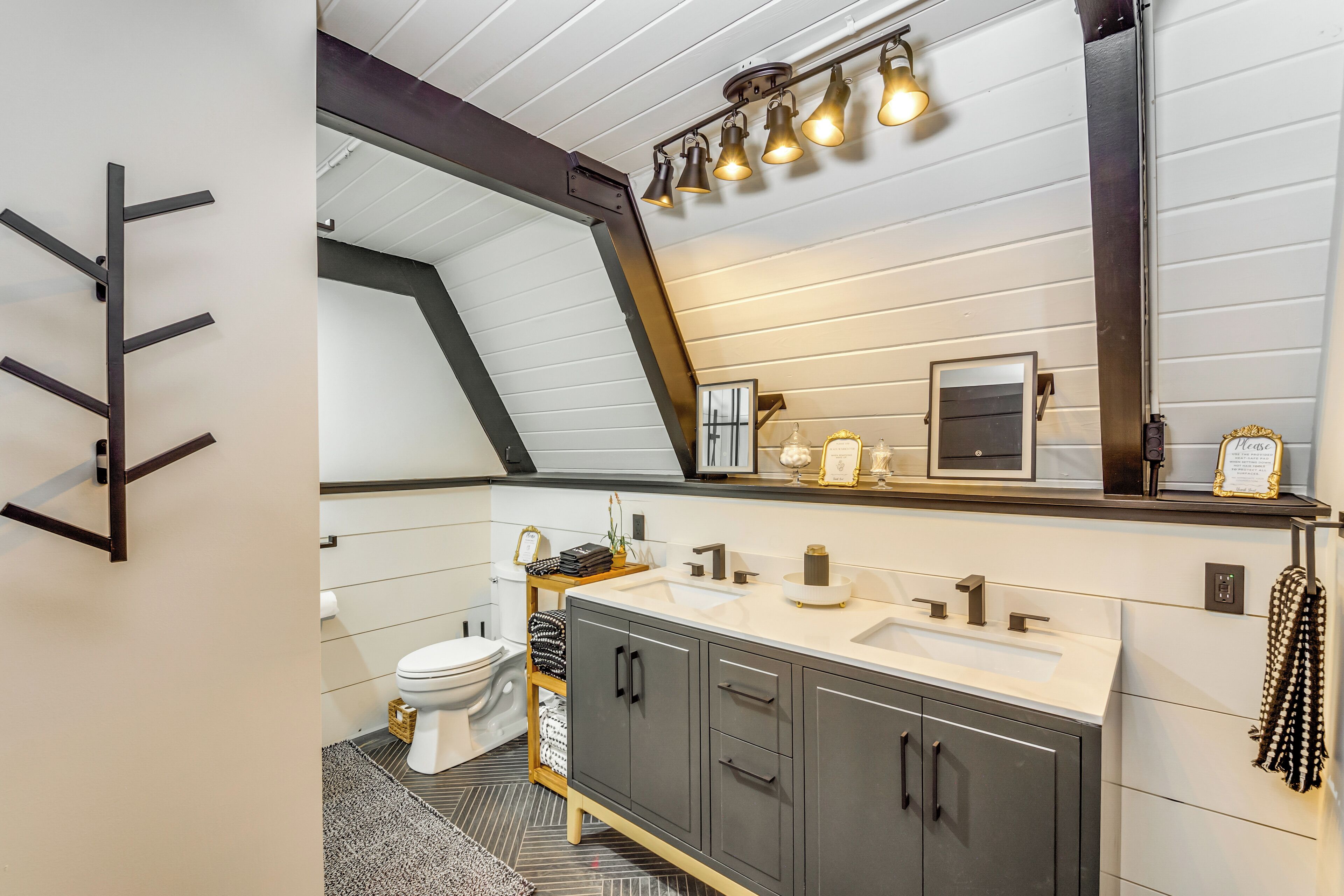 A modern bathroom with a white vanity, dark cabinets, a large mirror, and a ceiling light fixture.