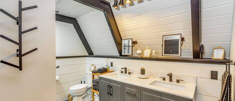 A modern bathroom with a white vanity, dark cabinets, a large mirror, and a ceiling light fixture.