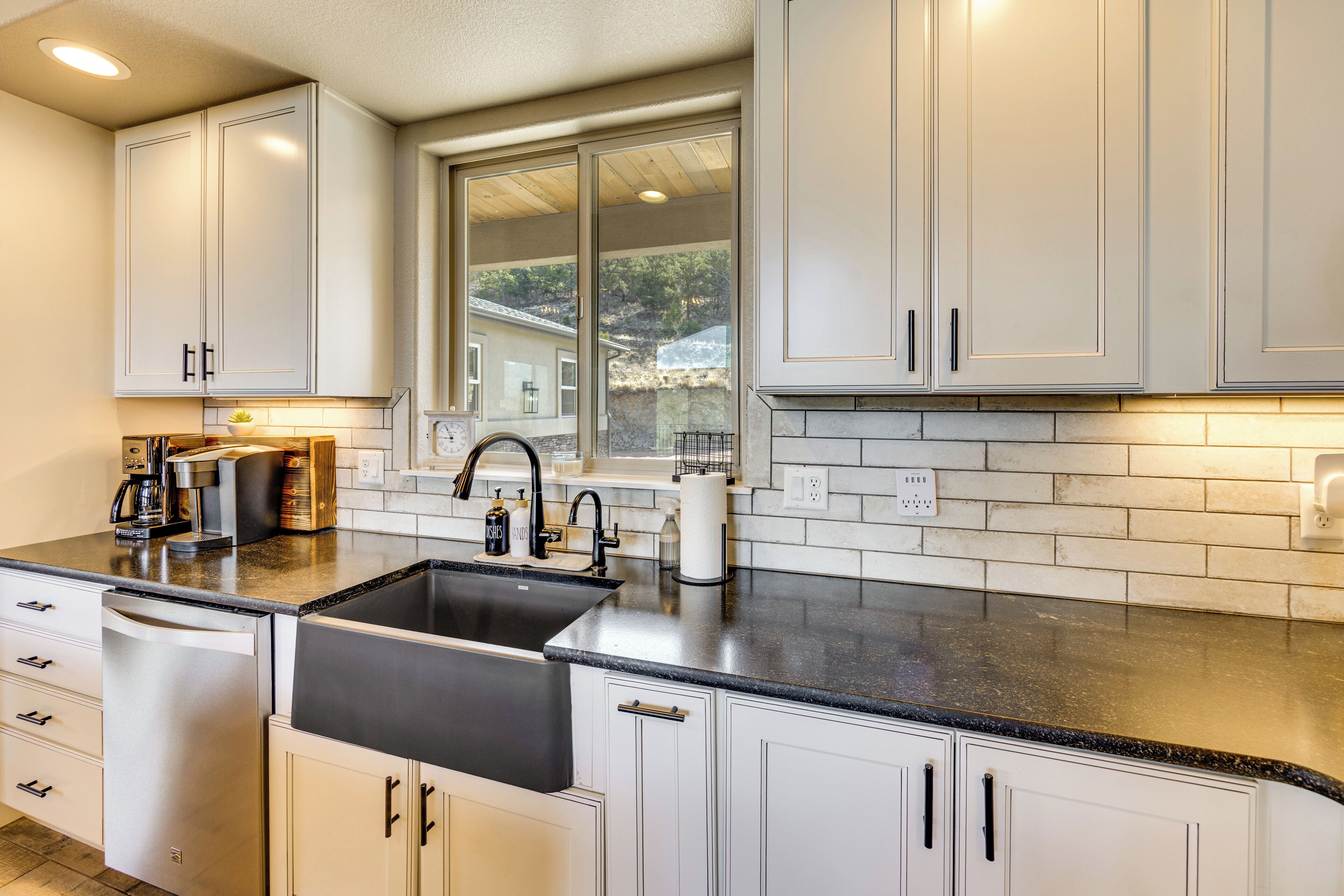 A modern kitchen with white cabinets, a black countertop, and a window overlooking a residential area.