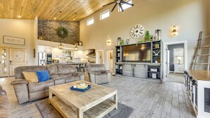 Un'ampia zona giorno con soffitto in legno, una parete d'accento in pietra, un orologio grande e una cucina sullo sfondo.