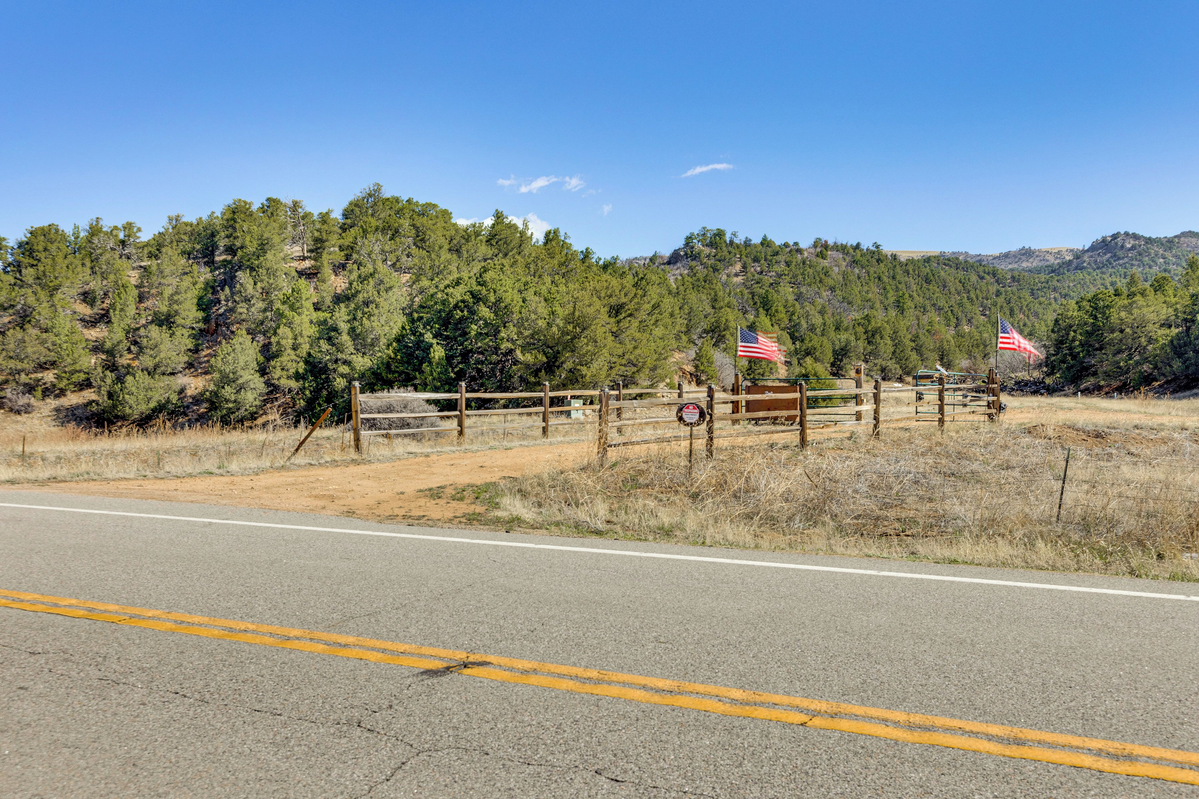 Eine Straße mit Holzzaun, zwei US-amerikanischen Flaggen und einer Berglandschaft im Hintergrund.