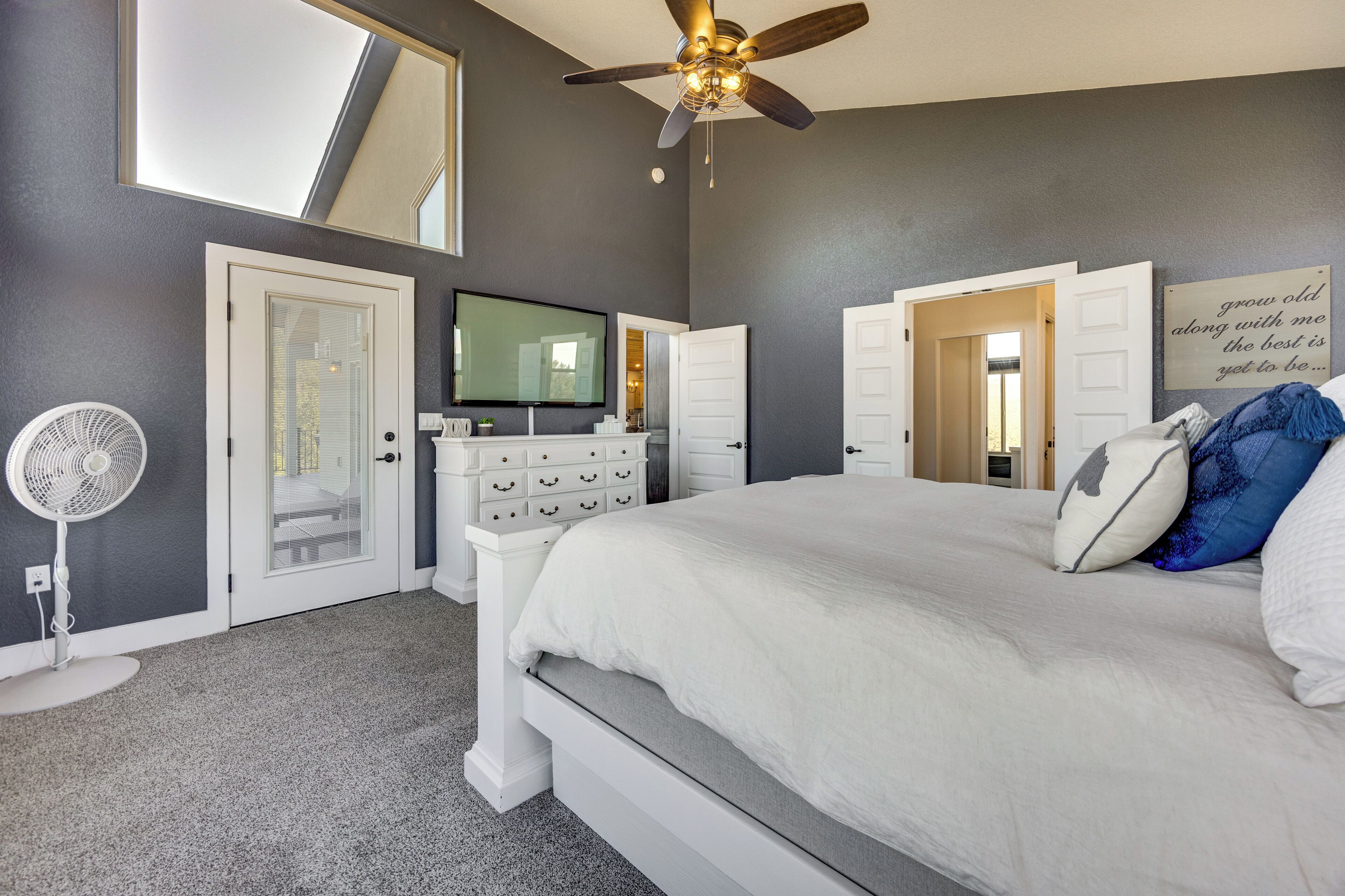 A bedroom with a bed, a ceiling fan, a TV, and a dresser.