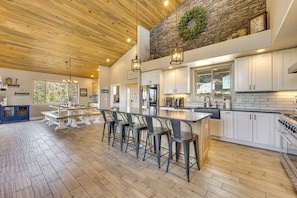 A spacious kitchen with a wooden ceiling, stone accent wall, and a large island with bar stools. - 200-acre Mtn Getaway Near the Arkansas River (Canon City)