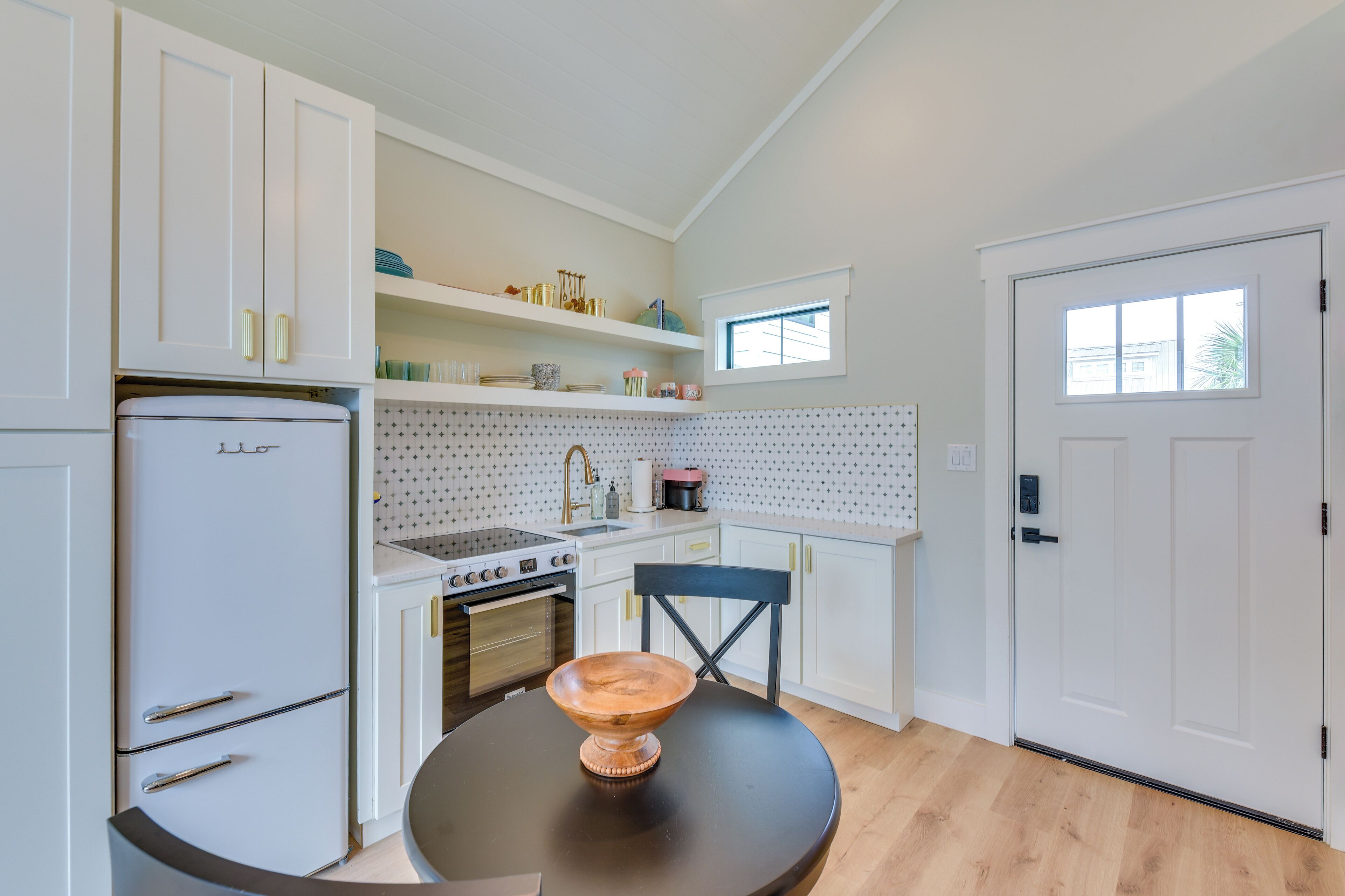 A compact kitchen with white cabinetry, a stove, and a dining table with a wooden bowl centerpiece.