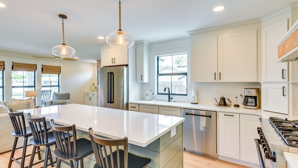 Moderni keittiö, jossa on suuri keittiösaareke, ruostumattomasta teräksestä valmistetut kodinkoneet ja riippuvalaisimet.