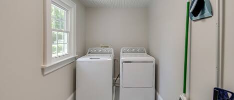 Une buanderie avec deux machines à laver blanches, une fenêtre et un balai.