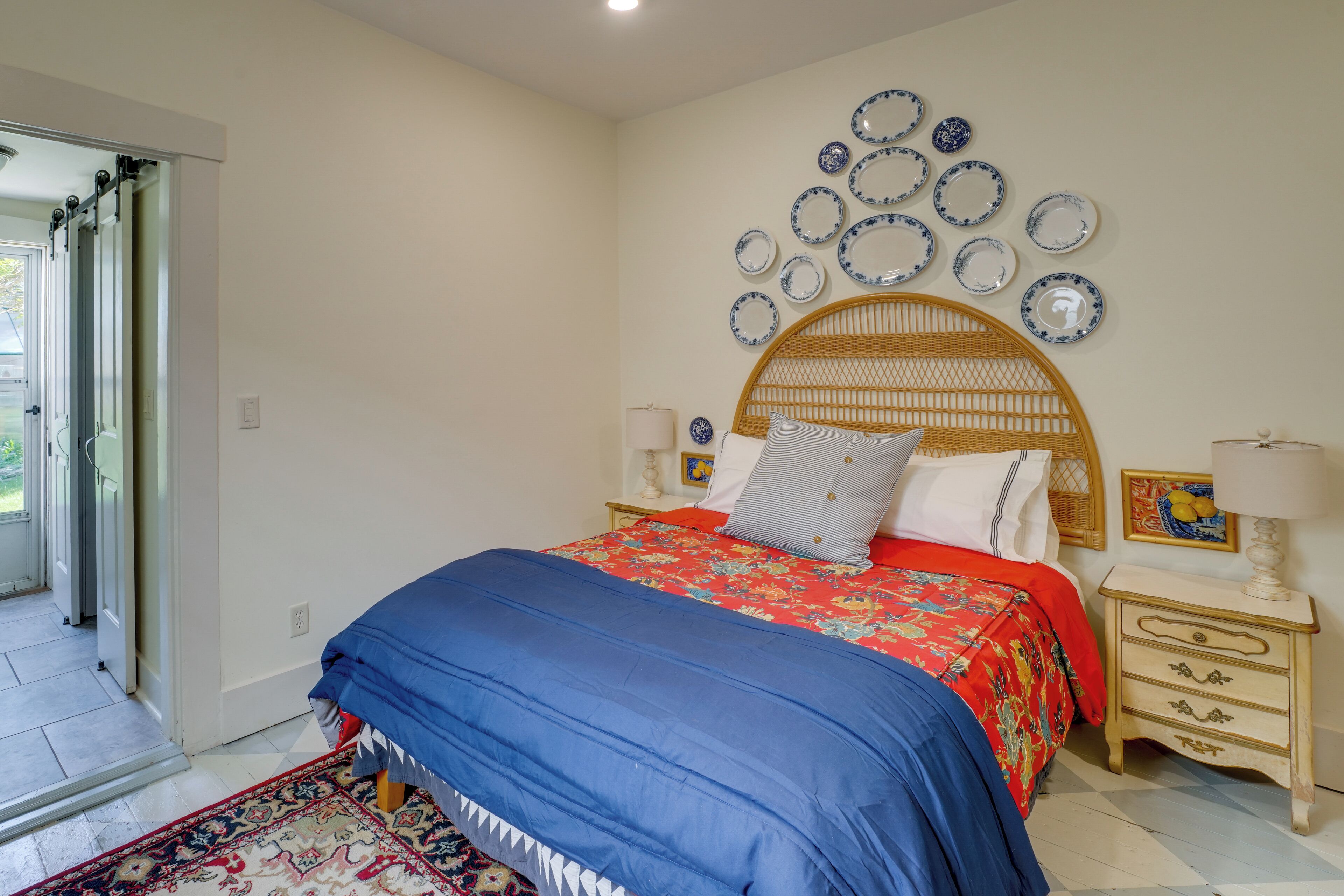 Un dormitorio con cama, una mesita de noche, una colección de platos en la pared y una puerta que da a un balcón.