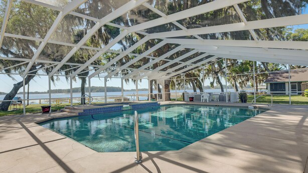 A pool area with a covered deck, a diving board, and a view of the water.