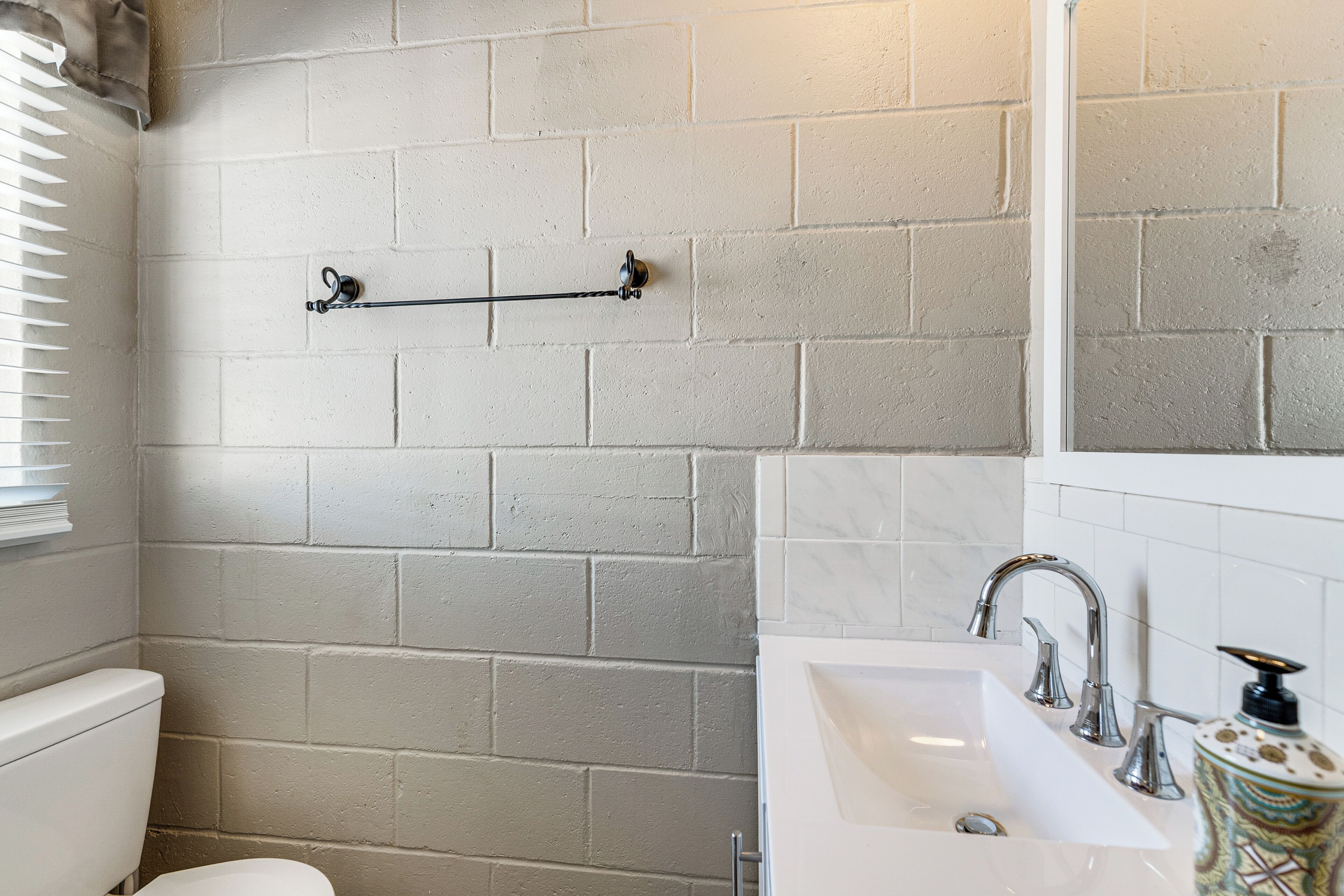 Ein Badezimmer mit weißem Waschbecken, einem Spiegel und einem Handtuchhalter an einer Ziegelwand.