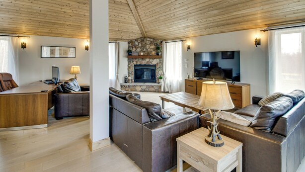 A modern living room with a stone fireplace, leather sofas, a wooden coffee table, and a television. - 40-acre Brook Park Retreat Near Lakes & Fishing! (Brook Park)