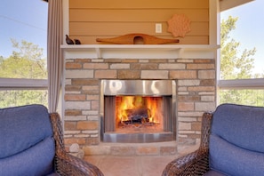 A stone fireplace with a fire, two wicker chairs, and a view of trees. - Chiricahua Birding Cabin By Cave Creek Canyon! (San Simon)