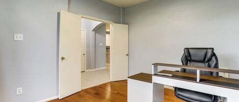 A room with a desk, chair, and a door leading to another room.