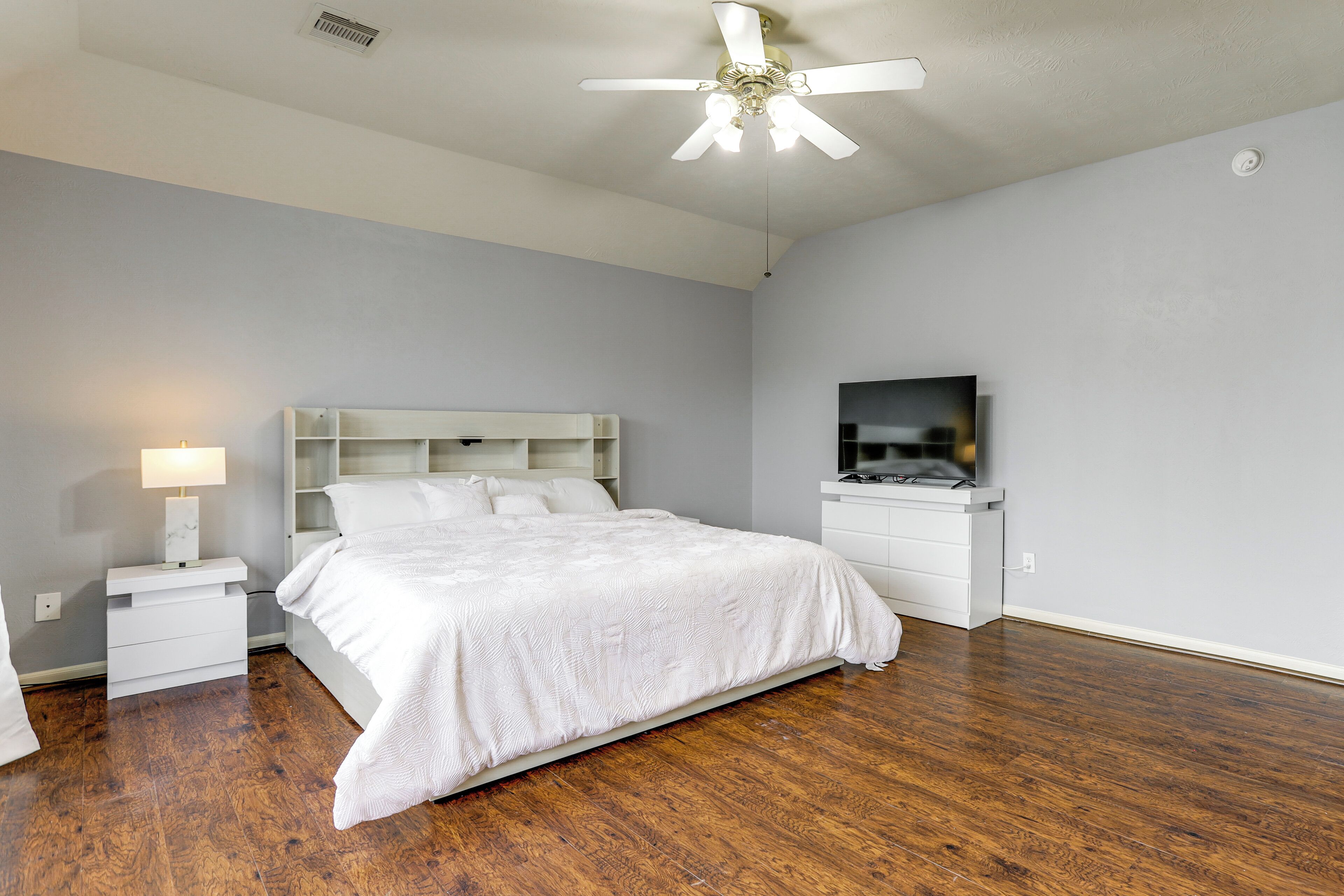 A bedroom with a bed, a nightstand, a TV, and a ceiling fan.