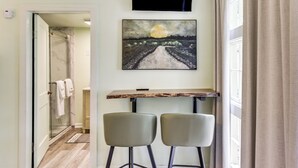 Un pasillo con una puerta de ducha de vidrio, un cuadro de un paisaje y una mesa con dos sillas.