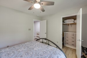 Une chambre à coucher comprenant un lit, un ventilateur de plafond, une armoire et une porte donnant sur un couloir.