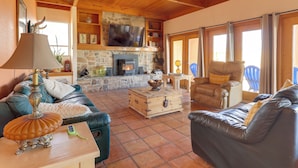 A cozy living room with a fireplace, leather sofas, a television, and a stone wall.