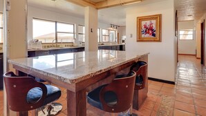 A kitchen with a large island, bar stools, and a tiled floor.