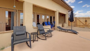 A covered outdoor area with chairs and a table, a wooden fence, and a building with large windows.