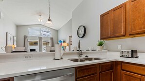 Una cocina moderna con lavavajillas, pileta, muebles de madera, un reloj y un tostador.