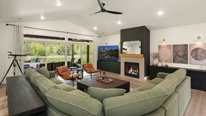 Een moderne woonkamer met een hoekbank, een open haard, een televisie en een balkon met buitenmeubels.