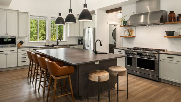Een moderne keuken met een centraal eiland, barkrukken, roestvrijstalen apparatuur en hanglampen.