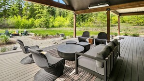 Een terras buiten met een overdekte zithoek, vuurplaats en uitzicht op een bebost landschap.