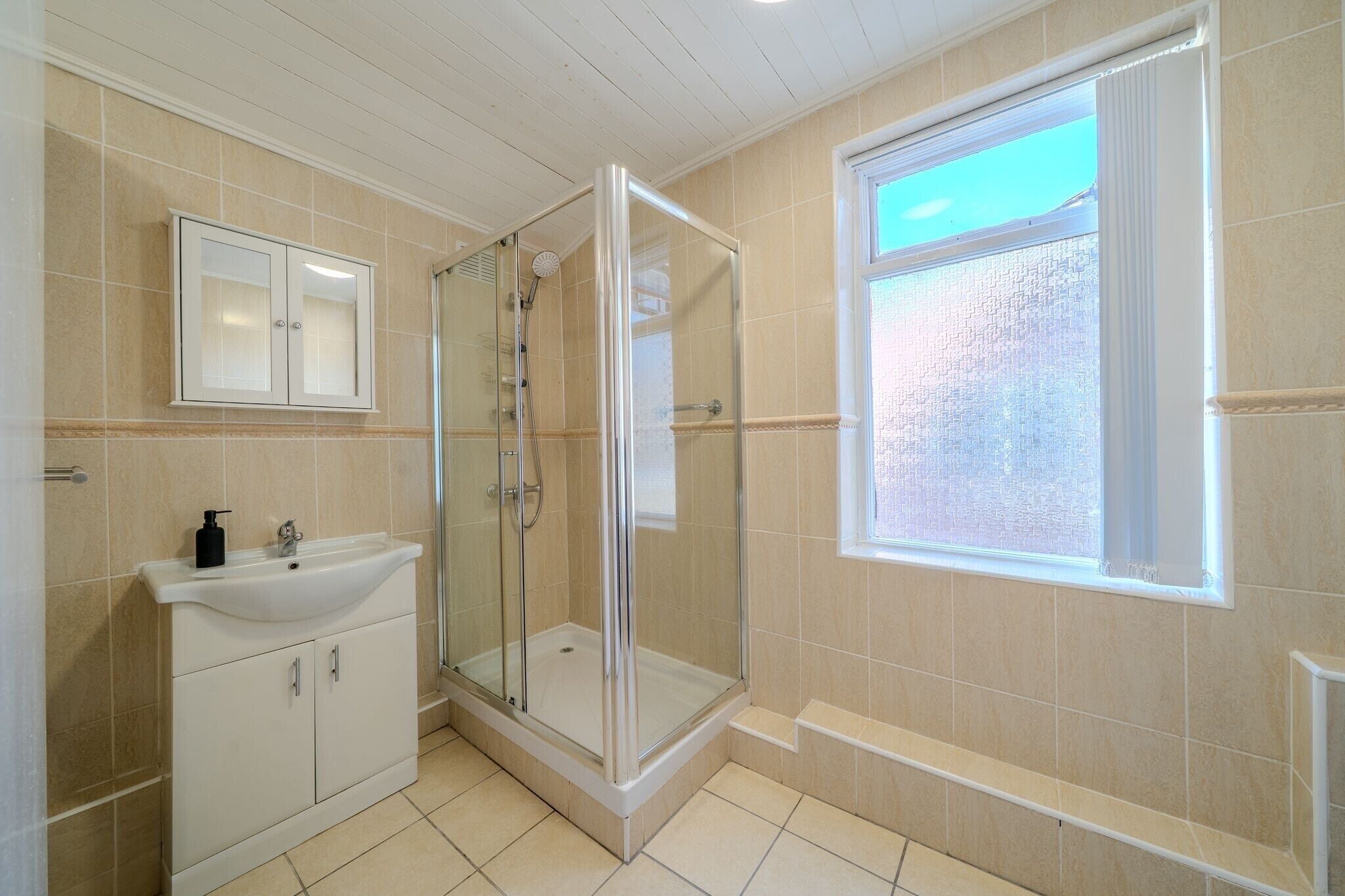 A bathroom with a shower, sink, and cabinet.
