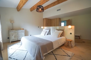 Ein Schlafzimmer mit einem Bett, Holzbalken, einem Nachttisch, einer Lampe und einem Spiegel.