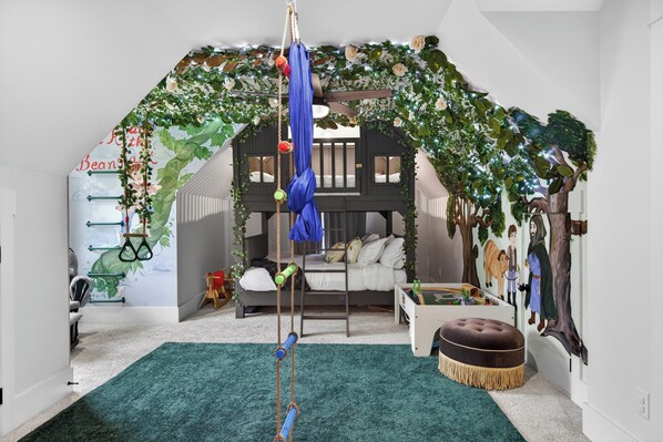 Een kamer met een hoogslaper, een schommel, een groen tapijt en een muurschildering.