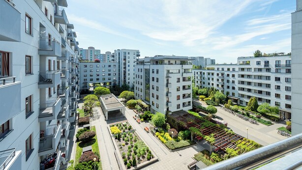 Un moderno complejo de apartamentos con varios balcones, un patio central con vegetación y un cielo despejado.