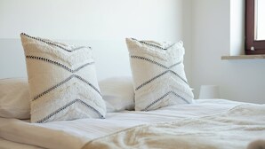 Una cama impecable con dos almohadones decorativos y una pared blanca al fondo.