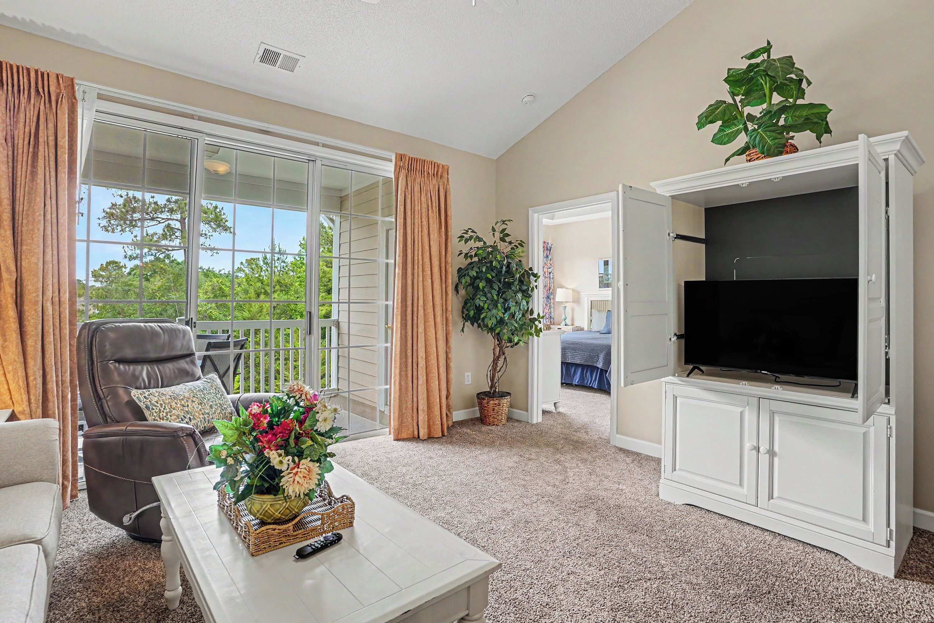 A living room with a TV, a sofa, a chair, a coffee table, and a plant.