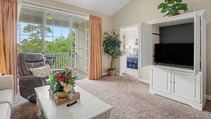 A living room with a TV, a sofa, a chair, a coffee table, and a plant. - Ironwood #1433 New on Program! Great Location and Lots of Amenities! (North Myrtle Beach)