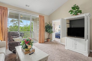 A living room with a TV, a sofa, a chair, a coffee table, and a plant. - Ironwood #1433 New on Program! Great Location and Lots of Amenities! (North Myrtle Beach)
