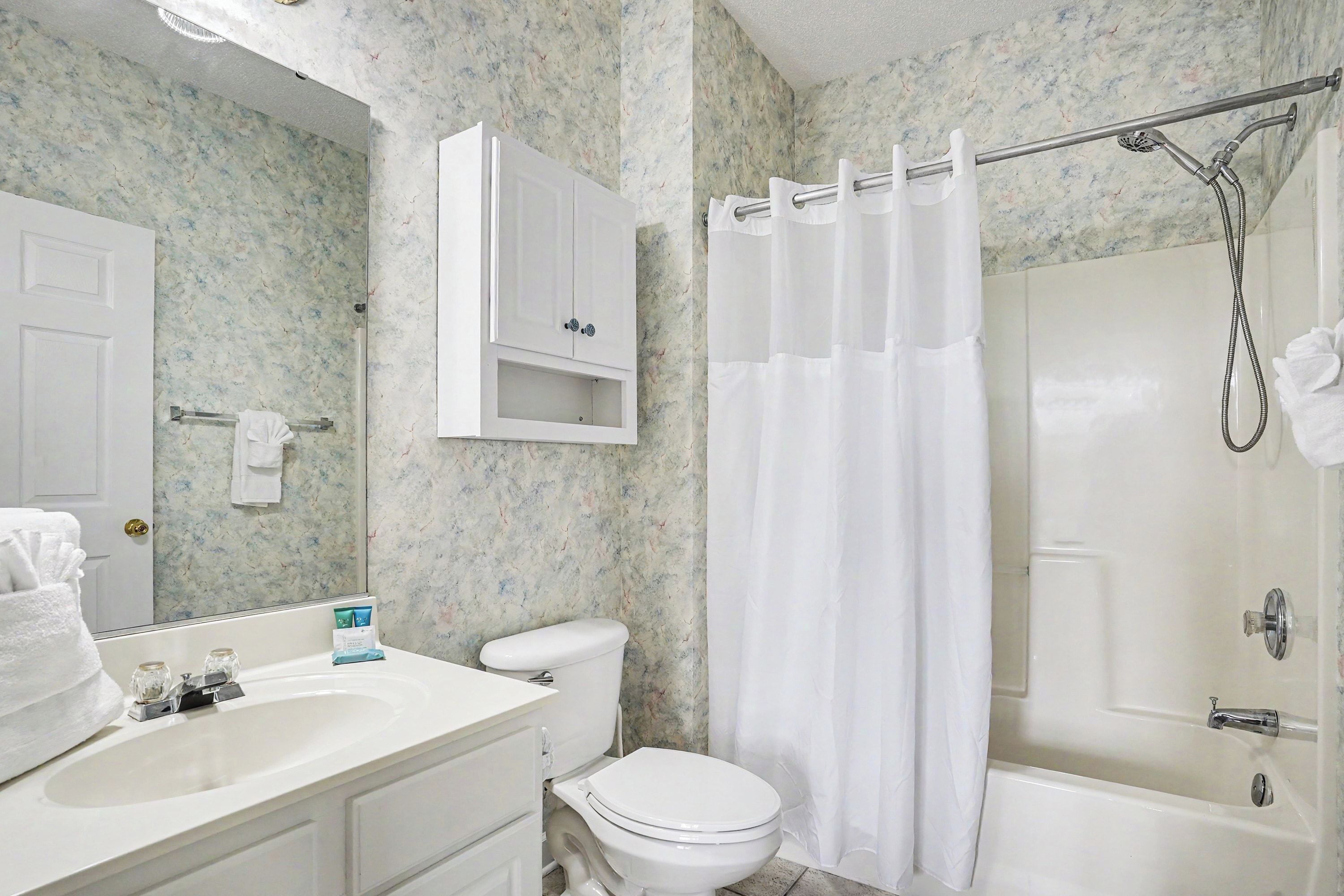 A bathroom with a white sink, toilet, and bathtub, a shower curtain, and a mirror above the sink.
