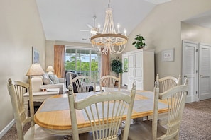 A dining area with a chandelier, wooden chairs, a table, and a view of the outdoors. - Ironwood #1433 New on Program! Great Location and Lots of Amenities! (North Myrtle Beach)