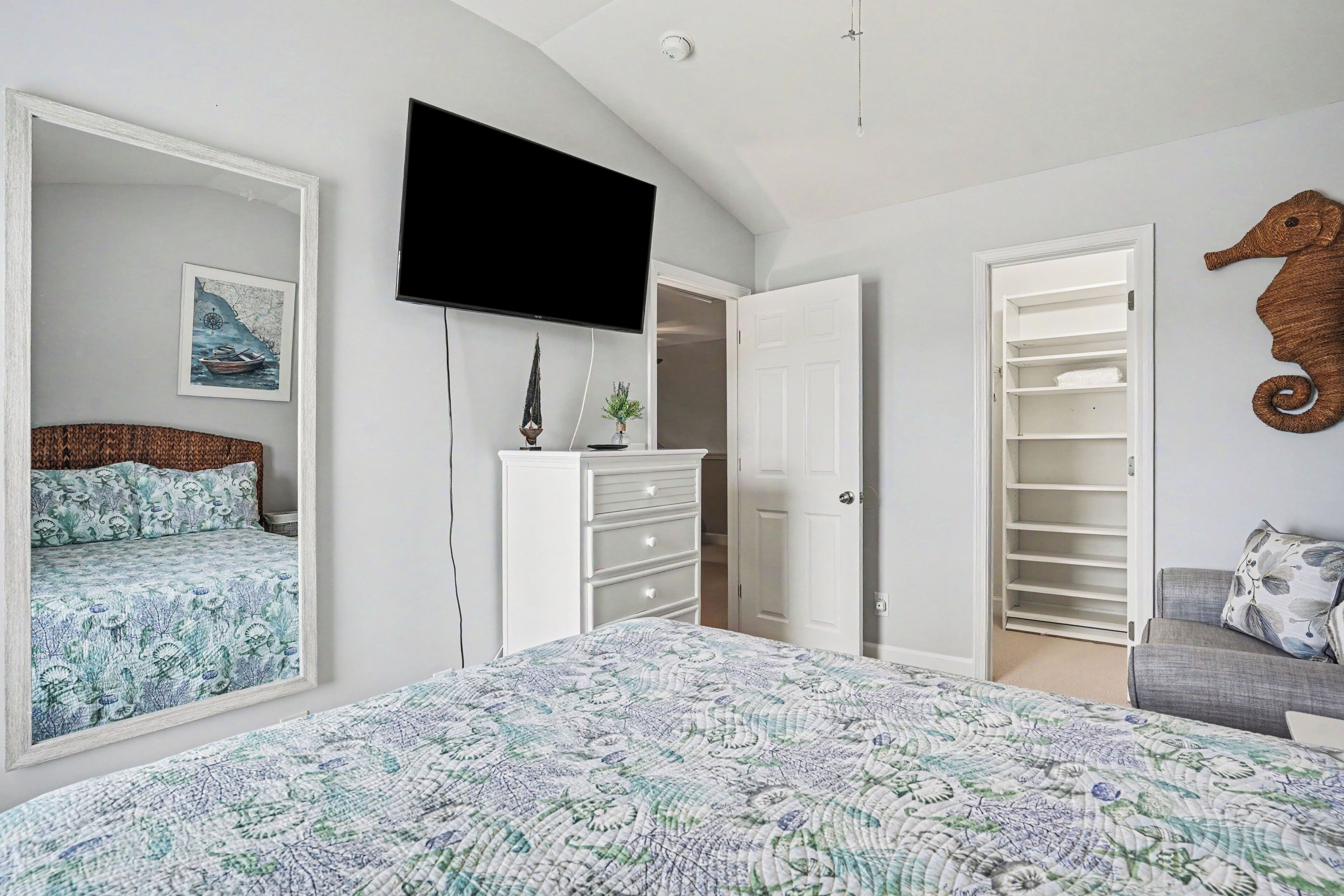 Une chambre à coucher comprenant un lit, une commode, un téléviseur, un placard et une décoration représentant un hippocampe.