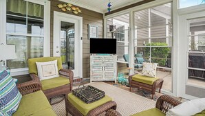 Un porche cubierto con muebles de mimbre, un televisor de pantalla plana y un aparador con objetos decorativos.