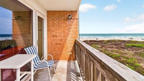 Balkon med udsigt over stranden, et bord og to stribede stole.