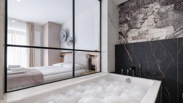 A modern bathroom with a large bathtub filled with bubbles, a mirror, and a wall with a marble pattern. - Love Story Studio with Jacuzzi Sopot (Sopot)