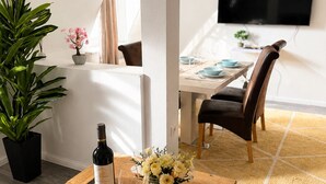 Un espace de vie moderne avec une table basse en bois, une plante en pot et un coin repas avec un téléviseur en arrière-plan.