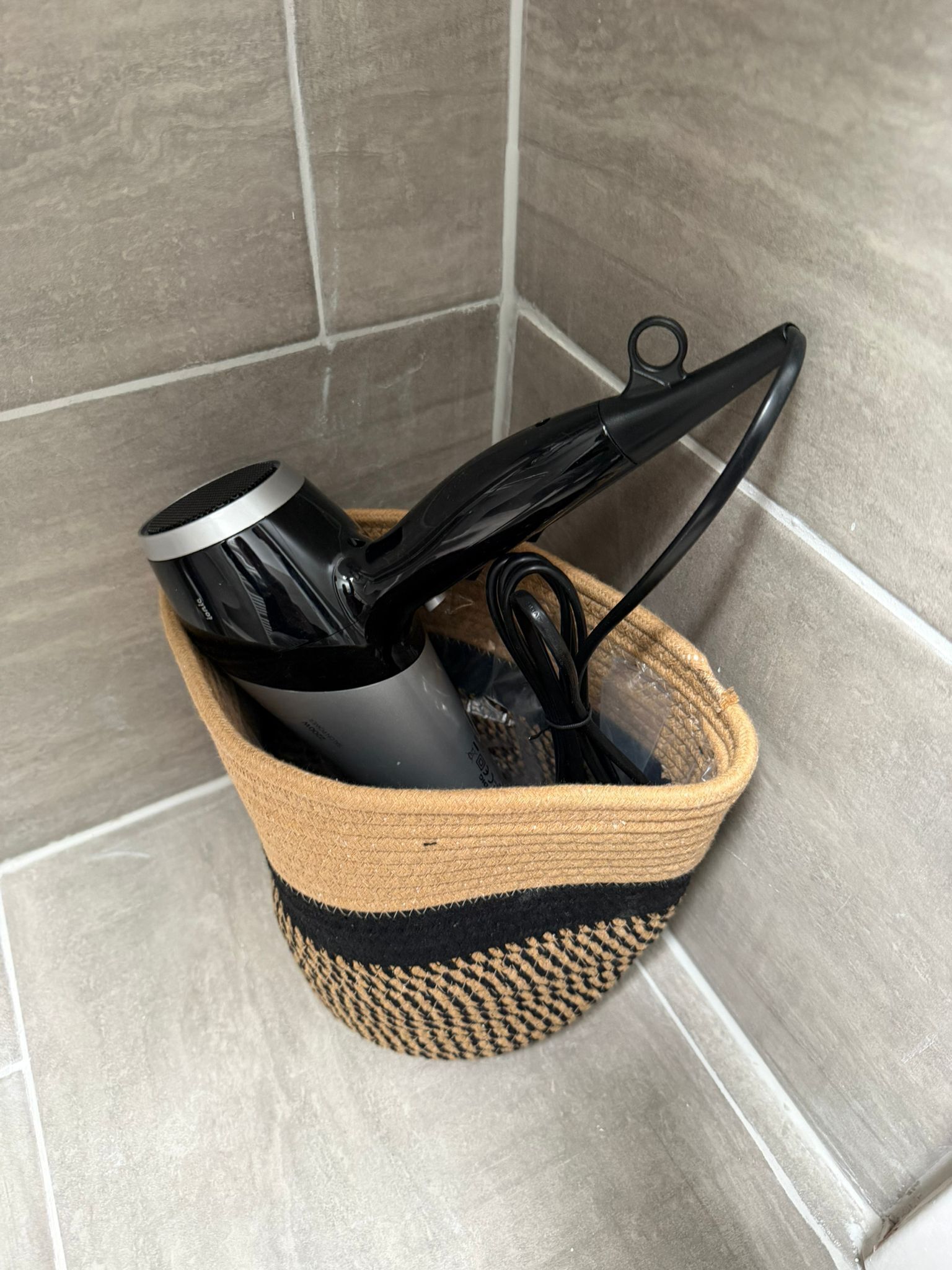 Un panier tressé contenant un objet cylindrique noir, qui pourrait être un haut-parleur, ainsi qu’un câble noir.