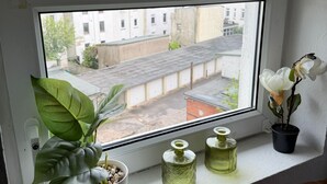 Une fenêtre donnant sur des immeubles, une plante en pot et deux vases en verre posés sur le rebord.