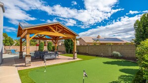 Ein Garten mit einer Holzpergola, einer Terrasse mit Gartenmöbeln, einem grünen Rasen und einer Backsteinmauer.
