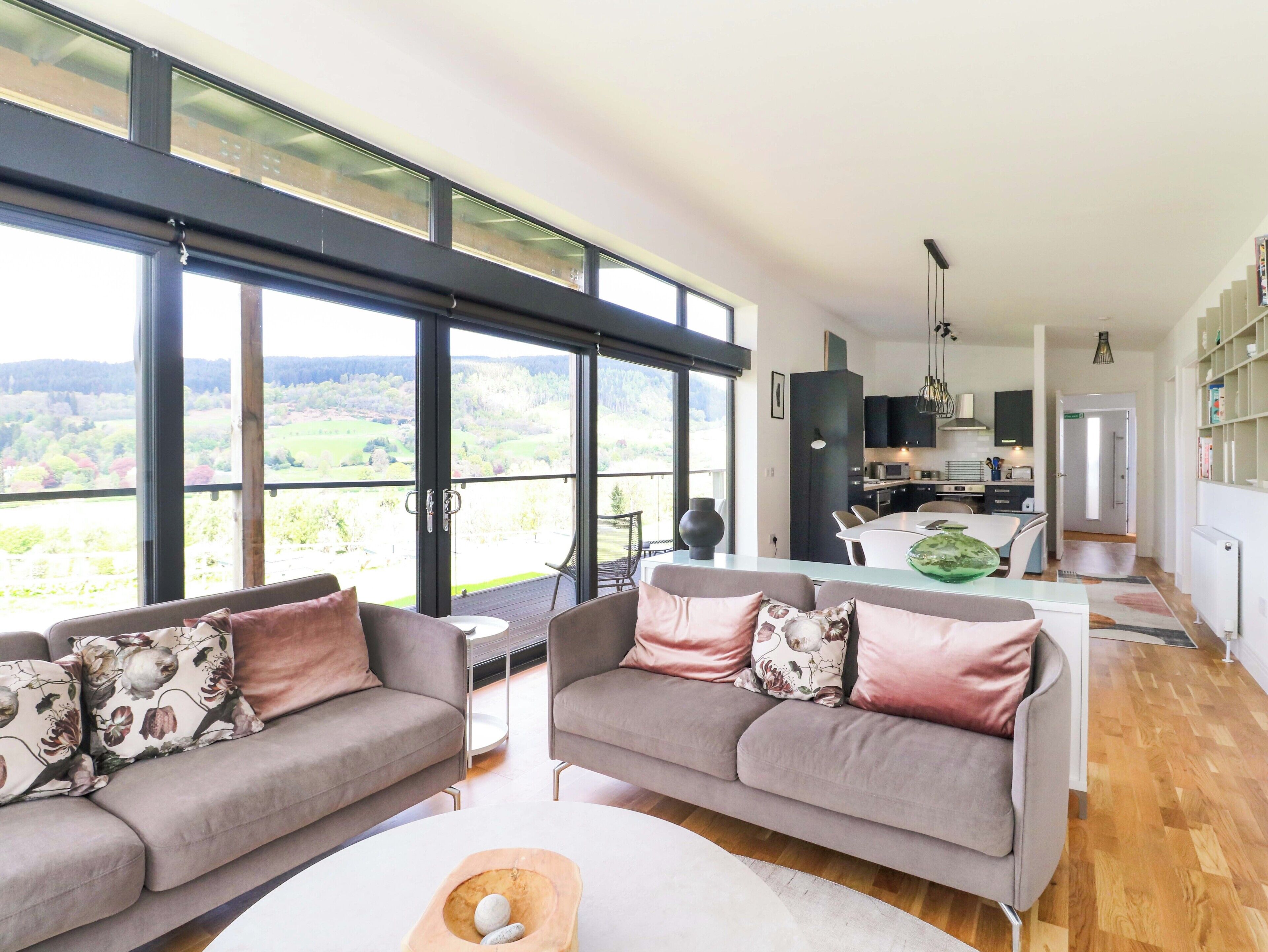 A modern living room with two grey sofas, a dining table, and a kitchen in the background.