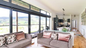 Una sala de estar moderna con dos sofás grises, una mesa de comedor y una cocina al fondo.