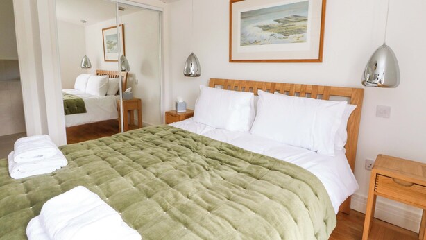Habitación de hotel con una cama, cabecero de madera, mesita de noche, espejo y un cuadro en la pared.