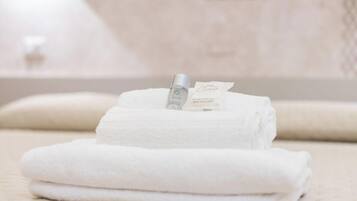 Des serviettes blanches, soigneusement pliées, et un flacon de savon sont posés sur une surface.