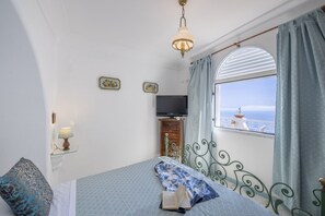 Ein Schlafzimmer mit einem Bett, einem Fernseher, einem Fenster mit Vorhängen und Meerblick.